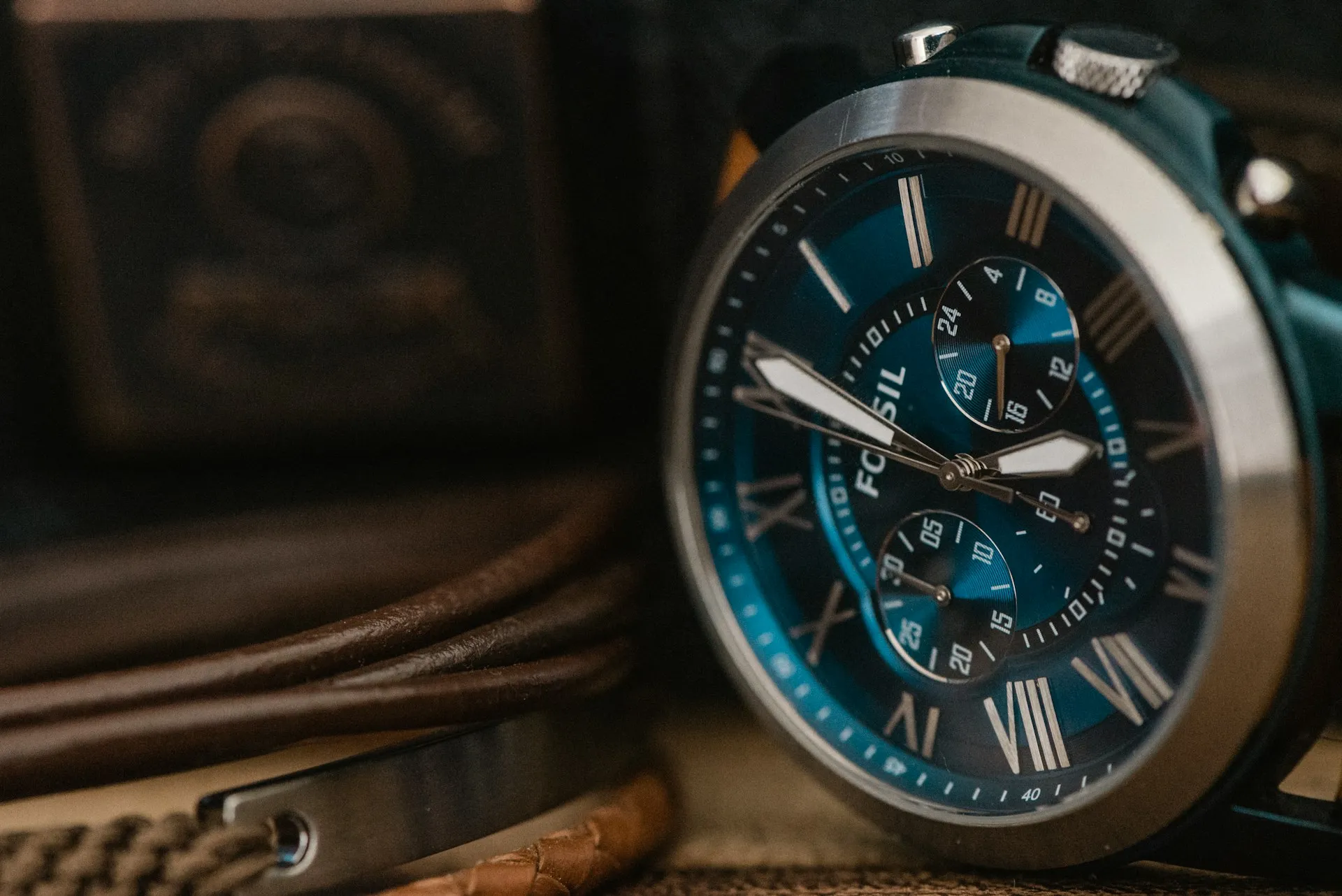 Stylish men's wristwatch Stylish men's wristwatch with a blue face and Roman numerals, placed on a leather surface with accessories.
