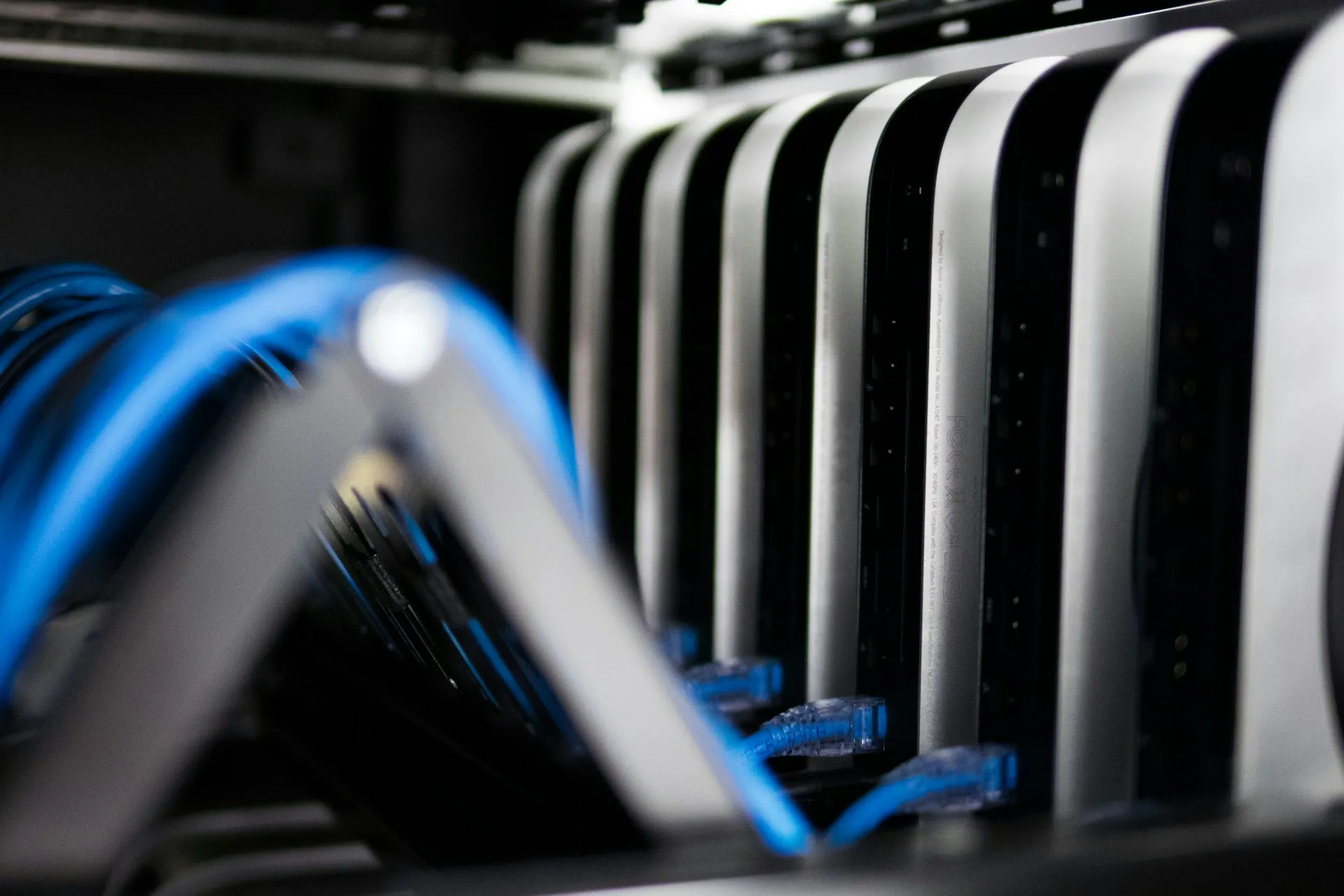 Networked Mac Mini servers Close-up of multiple networked Mac Mini servers connected with blue Ethernet cables in a data center rack.